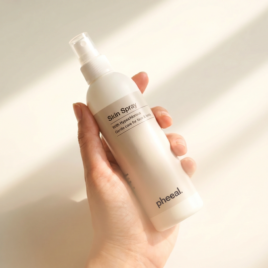Hand holding a bottle of Pheeal Skin Spray against a neutral background